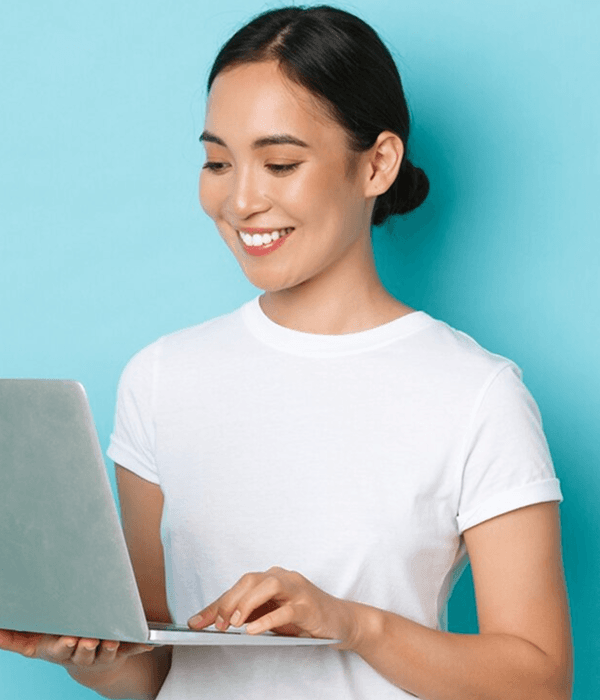 Smiling woman in white t-shirt holding and using a laptop against a light blue background.